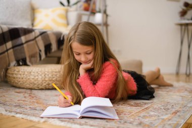 Dünya çapında koronavirüs salgını sırasında, kız evden çıkmadan okulda müfredatı öğreniyor. Yere yatar ve kalemle deftere yazar.