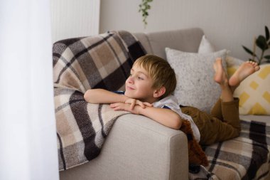 Evdeki odada kareli ekoseyle karnının üzerinde dinlenen güzel bir çocuğun portresi.