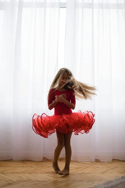 girl in red ball gown, dancing in room on floor, against backdrop of bright window