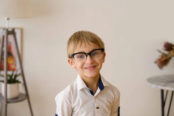 穿着眼镜和白衬衫的学龄前男孩在明亮的房间里微笑着看着摄像机 — 图库照片