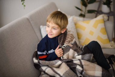 Gri koltukta oturan gülümseyen çocuk sıcak yünlü ekose kumaşa sarılmış evde.