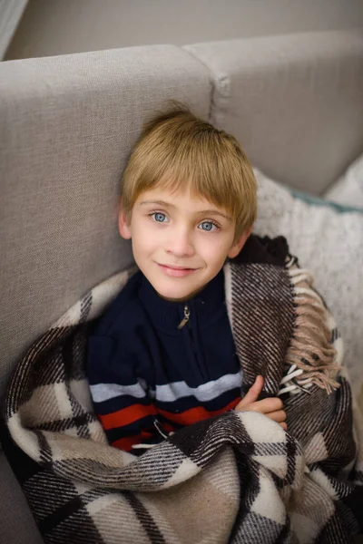 Χαμογελαστό Αγόρι Κάθεται Γκρι Καναπέ Τυλιγμένο Ζεστό Μαλλί Καρό Καρό — Φωτογραφία Αρχείου