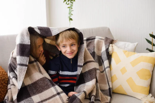 男の子と女の子 姉と弟はソファの上で毛布の下に座って 夢を見て 抱き合って 家の明るい部屋で — ストック写真