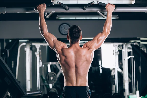 Atleta muscular fitness modelo masculino tirando hacia arriba en la barra horizontal en un gimnasio —  Fotos de Stock