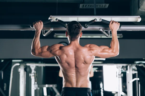 Athlete muscular fitness male model pulling up on horizontal bar in a gym — Stock Photo, Image