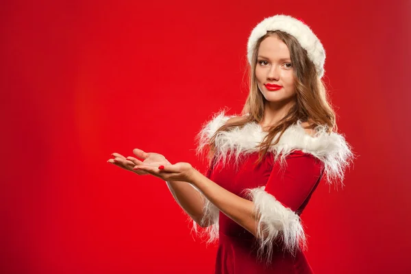 Natal, x-mas, inverno, conceito de felicidade - mulher sorridente em chapéu de Papai Noel ajudante com caixa de presente, de mãos dadas na frente dele, oferecendo um, sobre fundo vermelho . — Fotografia de Stock
