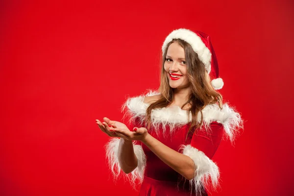 Natal, x-mas, inverno, conceito de felicidade - mulher sorridente em chapéu de Papai Noel ajudante com caixa de presente, de mãos dadas na frente dele, oferecendo um, sobre fundo vermelho . — Fotografia de Stock