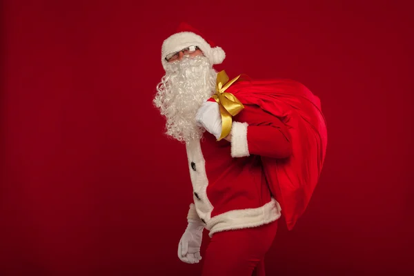 Weihnachtsmann mit großer Tasche auf Schulterbrille roter Hintergrund — Stockfoto