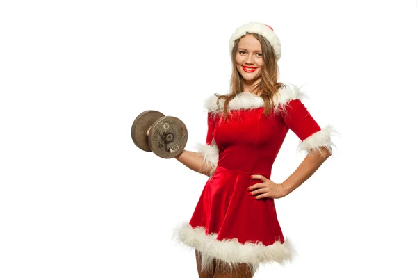 Рождество, Рождество, зима, концепция счастья - Бодибилдинг. Сильная женщина, тренирующаяся с гантелями в шляпе помощника Санты, изолированная на белом фоне. Мускулистая блондинка — стоковое фото