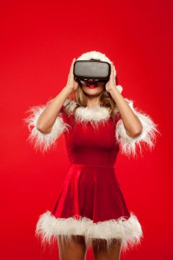 Noel, x-mas, kış, mutluluk kavramı - Noel Baba Yardımcısı uzun saçlı güzel genç esmer kırmızı arka plan üzerinde giyen sanal gerçeklik kulaklık şapka