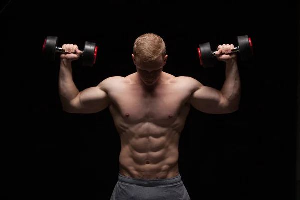 Handsome power man fitness-model with six packs is training with dumbbells, isolated on black background with copyspace — Stock Photo, Image