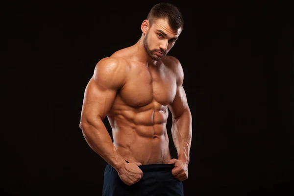 Sterke atletische Man - Fitness Model weergegeven: Torso met zes pack abs. staat rechte en zet zijn handen in broek. geïsoleerd op zwarte achtergrond met copyspace. — Stockfoto