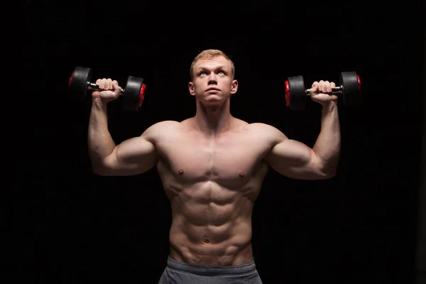 Handsome power man fitness-model with six packs is training with dumbbells, isolated on black background with copyspace — Stock Photo, Image