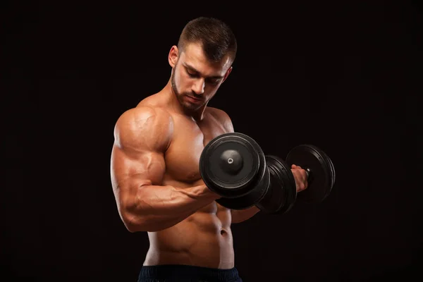 М'язистий красивий чоловік тренується з гантелями в спортзалі. ізольовані на чорному фоні з копійкою — стокове фото