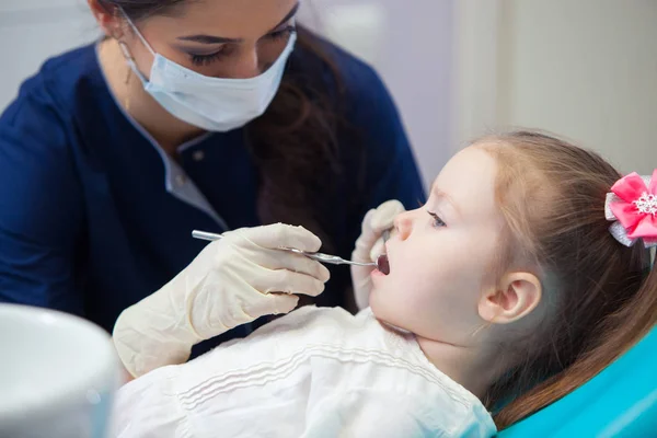 Dentista feminino em máscara trata dentes menina — Fotografia de Stock