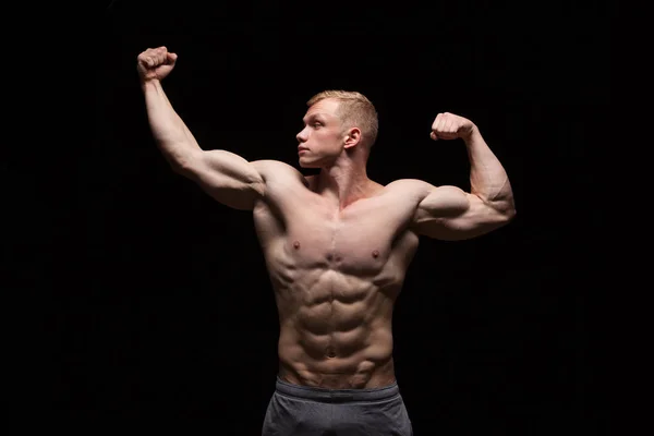 Athletic handsome man fitness-model is showing six pack abs and looking on the left. isolated on black background with copyspace — Stock Photo, Image