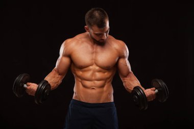 Eğitim salonunda dumbbells ile kas yakışıklı adamdır. siyah arka plan ile boşaltmak izole