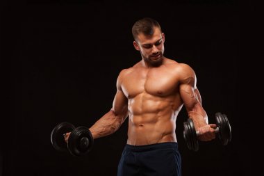 Spor salonunda yakışıklı atletik erkek bir spor salonunda dumbbells ile kasları yukarı pompalıyor. Fitness kas vücut üzerinde koyu arka plan izole.