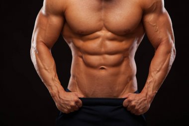 Güçlü adam atletik - Fitness modeli gösteren gövde altı bohça abs. ile düz duruyor ve pantolon içinde ellerini koyar. siyah arka plan ile boşaltmak izole
