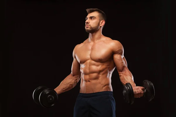 Spor salonunda yakışıklı atletik erkek bir spor salonunda dumbbells ile kasları yukarı pompalıyor. Fitness kas vücut üzerinde koyu arka plan izole. — Stok fotoğraf