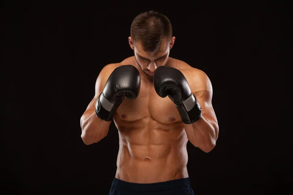 М'язова молода людина з досконалим тулуба з шести pack abs, боксерські рукавички показує різні рухи і вражає ізольовані на чорному тлі з copyspace — стокове фото