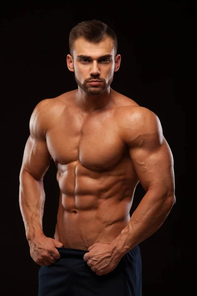 Hombre atlético fuerte - Modelo de fitness que muestra el torso con seis abdominales paquete. está derecho y pone las manos en los pantalones. aislado sobre fondo negro con copyspace —  Fotos de Stock