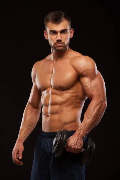 Hombre atlético de poder guapo con mancuerna está mirando hacia adelante con confianza. Culturista fuerte con seis pack, abdominales perfectos, hombros, bíceps, tríceps y pecho Aislado sobre fondo negro con — Foto de Stock