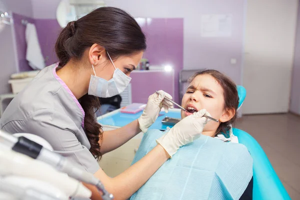 Nahaufnahme eines hübschen kleinen Mädchens, das seinen Mund weit öffnet, während der Zahnarzt ihre Zähne behandelt — Stockfoto