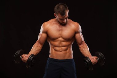 Eğitim salonunda dumbbells ile kas yakışıklı adamdır. siyah arka plan ile boşaltmak izole