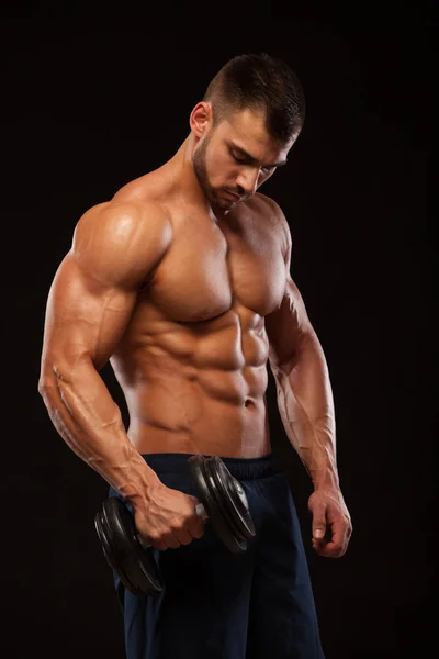 Hombre atlético de poder guapo con mancuerna está mirando hacia adelante con confianza. Culturista fuerte con seis pack, abdominales perfectos, hombros, bíceps, tríceps y pecho Aislado sobre fondo negro con — Foto de Stock