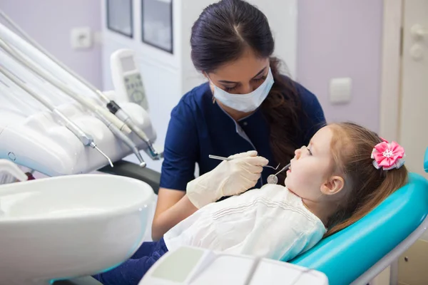 Dentista femenino en máscara trata los dientes niña — Foto de Stock