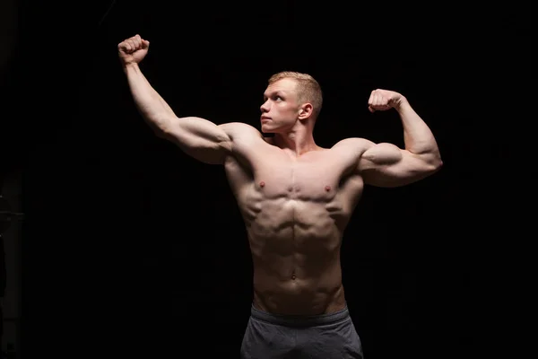 Athletic handsome man fitness-model is showing six pack abs and looking on the left. isolated on black background with copyspace — Stock Photo, Image