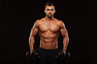 Eğitim salonunda dumbbells ile kas yakışıklı adamdır. siyah arka plan ile boşaltmak izole