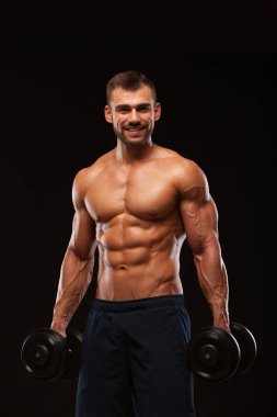 Spor salonunda yakışıklı atletik erkek bir spor salonunda dumbbells ile kasları yukarı pompalıyor. Fitness kas vücut üzerinde koyu arka plan izole.