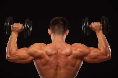 Kaslı erkek model vücut geliştirmeci geri döndü dumbbells ile yapıyor. Siyah arka plan ile boşaltmak izole