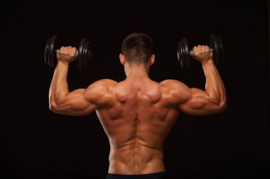 Kaslı erkek model vücut geliştirmeci geri döndü dumbbells ile yapıyor. Siyah arka plan ile boşaltmak izole