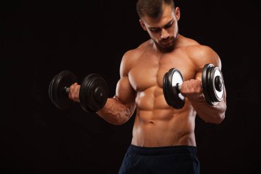 Eğitim salonunda dumbbells ile kas yakışıklı adamdır. siyah arka plan ile boşaltmak izole