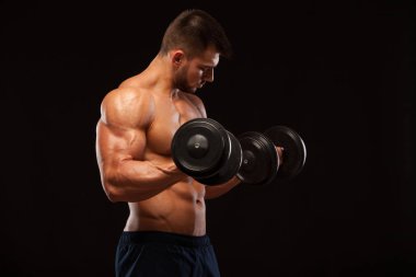 Eğitim salonunda dumbbells ile kas yakışıklı adamdır. siyah arka plan ile boşaltmak izole