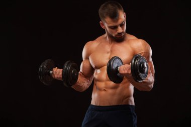 Eğitim salonunda dumbbells ile kas yakışıklı adamdır. siyah arka plan ile boşaltmak izole