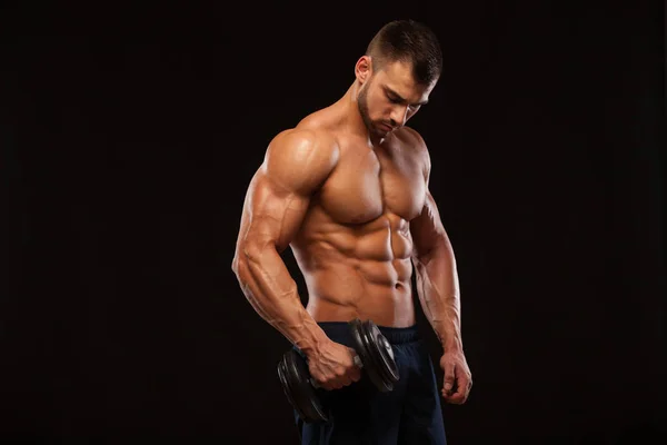 Handsome power athletic man with dumbbell is confidently looking forward. Strong bodybuilder with six pack, perfect abs, shoulders, biceps, triceps and chest Isolated on black background with — Stock Photo, Image