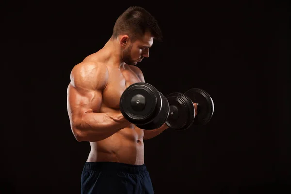 Hombre musculoso guapo está entrenando con pesas en el gimnasio. aislado sobre fondo negro con copyspace — Foto de Stock