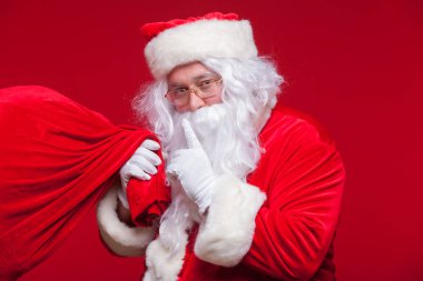 Noel Baba portresi ile işaret parmağı ağzında tarafından tutulması ve kameraya bakarak büyük kırmızı çuval