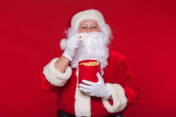 Babbo Natale tradizionale guardare la TV, mangiare popcorn. Natale. Sfondo rosso. emozioni paura sorpresa — Foto Stock