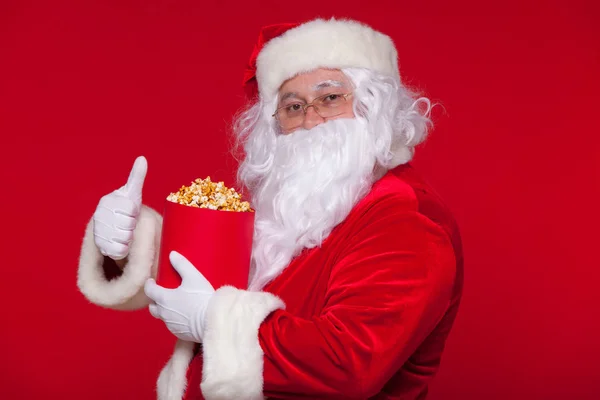 O Pai Natal tradicional a ver televisão, a comer pipocas. No Natal. Fundo vermelho. emoções medo surpresa — Fotografia de Stock