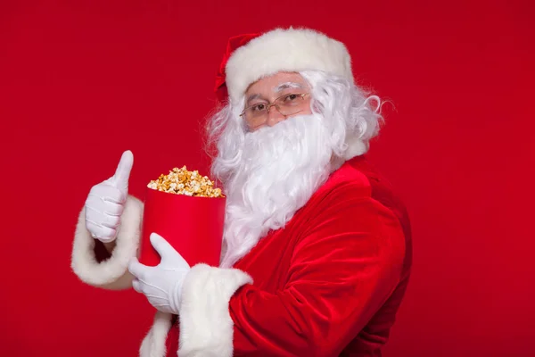 O Pai Natal tradicional a ver televisão, a comer pipocas. No Natal. Fundo vermelho. emoções medo surpresa — Fotografia de Stock