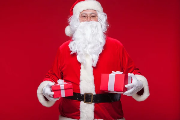 Christmas. Photo Santa Claus giving xmas present and looking at camera, on a red background — Stock Photo, Image