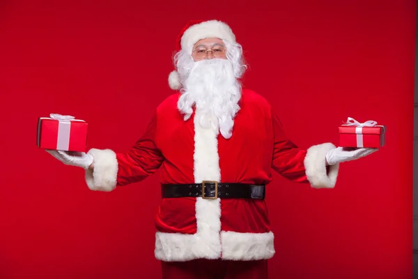 Weihnachten. photo santa claus macht Weihnachtsgeschenk und blickt in die Kamera, auf rotem Hintergrund — Stockfoto