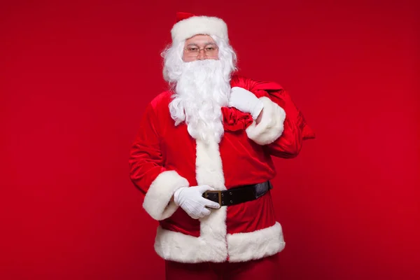 Navidad. santa claus con gran bolso en el hombro es sobre fondo rojo —  Fotos de Stock