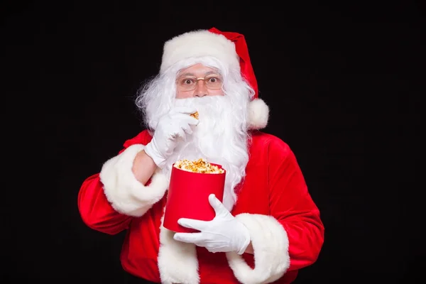 Natale. Foto di Babbo Natale mano guantata Con un secchio rosso con popcorn, su uno sfondo nero — Foto Stock