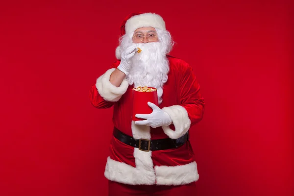 Traditionelle Weihnachtsmann vor dem Fernseher, essen Popcorn. Weihnachten. roter Hintergrund. Emotionen fürchten Überraschung — Stockfoto